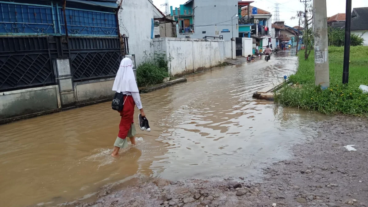 MENGGENANG: Salah satu siswa melintasi jalan yang tergenang banjir akibat luapan Sungai Cimande, di Desa Cihan