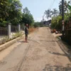 MENUNJUKAN: Salah seorang warga (Iwan) menunjukan kondisi jalan yang rusak, di Desa Jatihurip, baru-baru ini.
