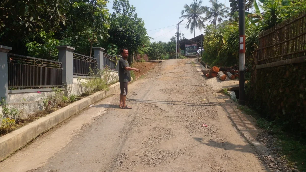 MENUNJUKAN: Salah seorang warga (Iwan) menunjukan kondisi jalan yang rusak, di Desa Jatihurip, baru-baru ini.