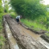 MEMPRIHATINKAN: Seorang warga sedang memperbaiki jalan yang terendam banjir karena kondisi jalan yang menuju M