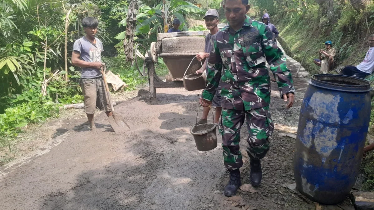 BERSINERGI: Babinsa Desa Tanjungwangi Sertu Sigit saat membantu warga memperbaiki jalan, Senin (10/6).