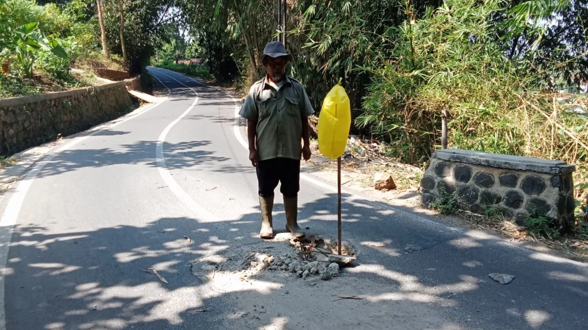 TUNJUKAN: Salah seorang petugas kebersihan Irin (54) saat menunjukan jalan berlubang di Desa Sawahdadap, Senin