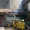 Para petugas pemadam kebakaran tengah memadamkan api yang melahap dua bangunan madrasah